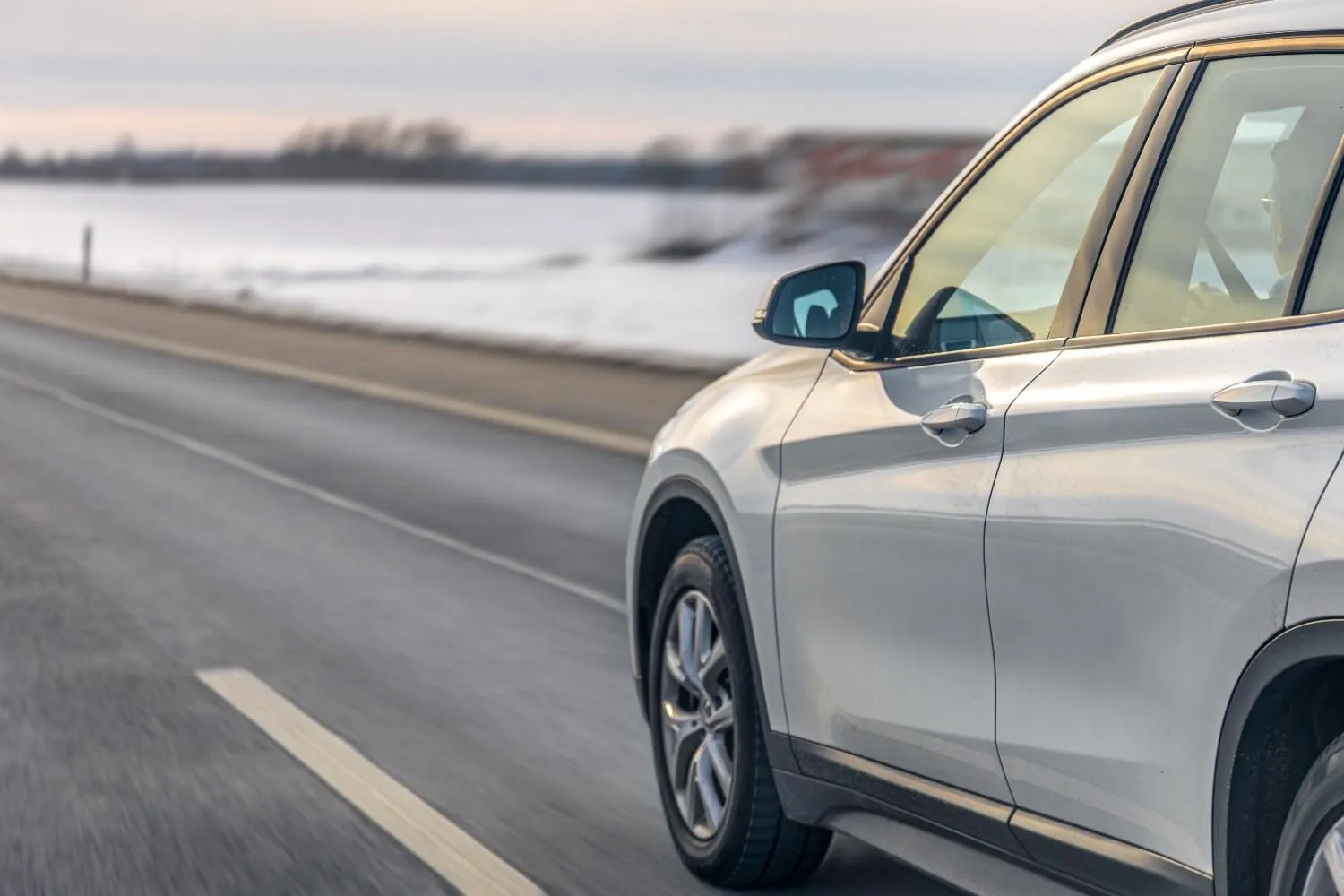A silver SUV driving along a clear highway past snowy fields