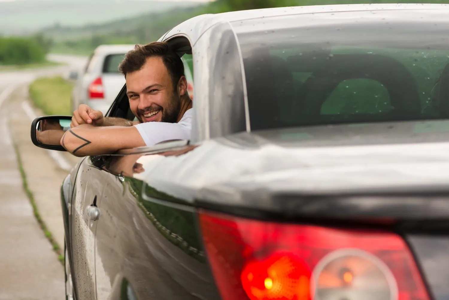 A smiling driver leaning out of his car window on a quiet country road